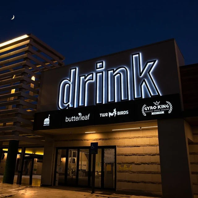 Illuminated Drink channel letters above a storefront facade at night